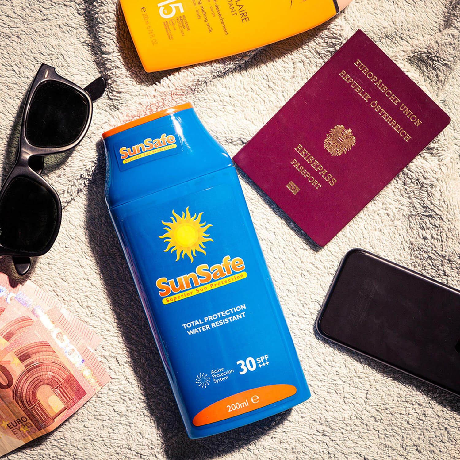 Auf dem Handtuch liegen Sonnencreme, ein Reisepass, eine Sonnenbrille, 10€-Scheine und ein Handy.