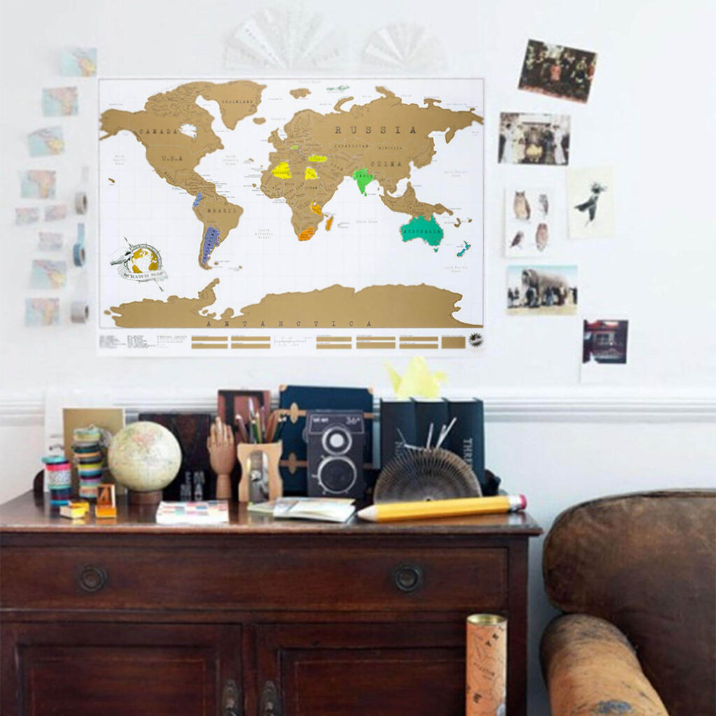 An der Zimmerwand über einer Kommode hängt eine Weltkarte mit goldenen Kontinenten - die bereisten Regionen sind freigerubbelt und erscheinen in bunten Farben - eine schöne Geschenkidee für Weltenbummler.