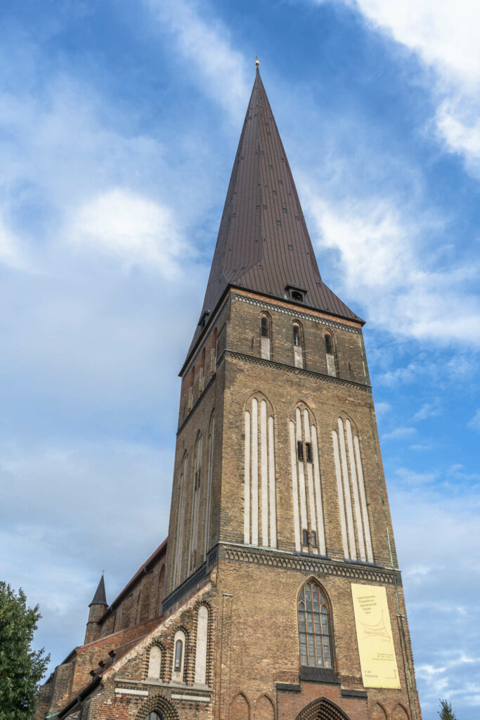 Die Rostocker Petrikirche erhebt sich in den strahlend blauen Himmel mit weißen Wolken, die braunen Backsteine sieht man aus der Froschperspektive.