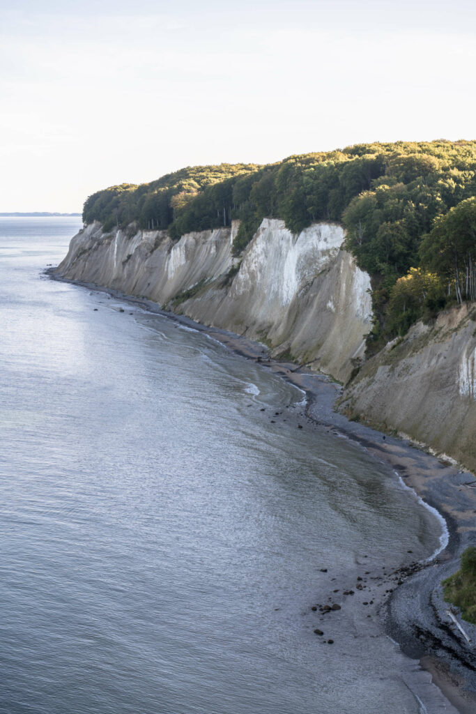 Vom Hochuferweg auf Rügen blickt man auf die kreideweiße Steilküste, die oben mit Gebüsch bewachsen ist, unten liegt das Meer.