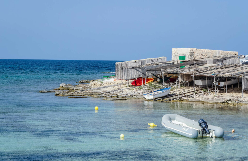 Hübsche Fischerhütten und Trockendocks aus Holz liegen malerisch in der Bucht von Es Pujol auf Formentera.