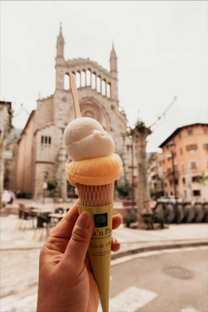 Auf dem Plaça Mercat Fet a Sóller auf Mallorca genießt Reisebloggerin Tatiana Eis in der Waffel, die Kirche Sant Bartomeu im Hintergrund.