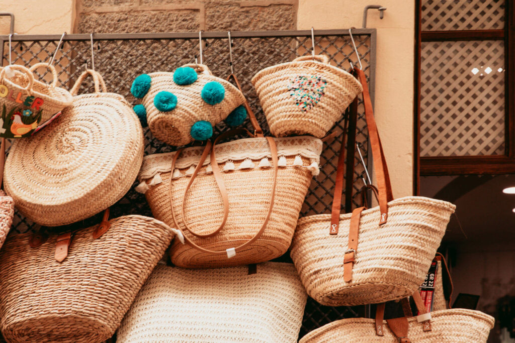 Mehrere Strohtaschen verschiedener Größen und Designs, die an einem Gitter zum Verkauf im Alameda Shop hängen, laden zum Shoppen in Sóller auf Mallorca ein.