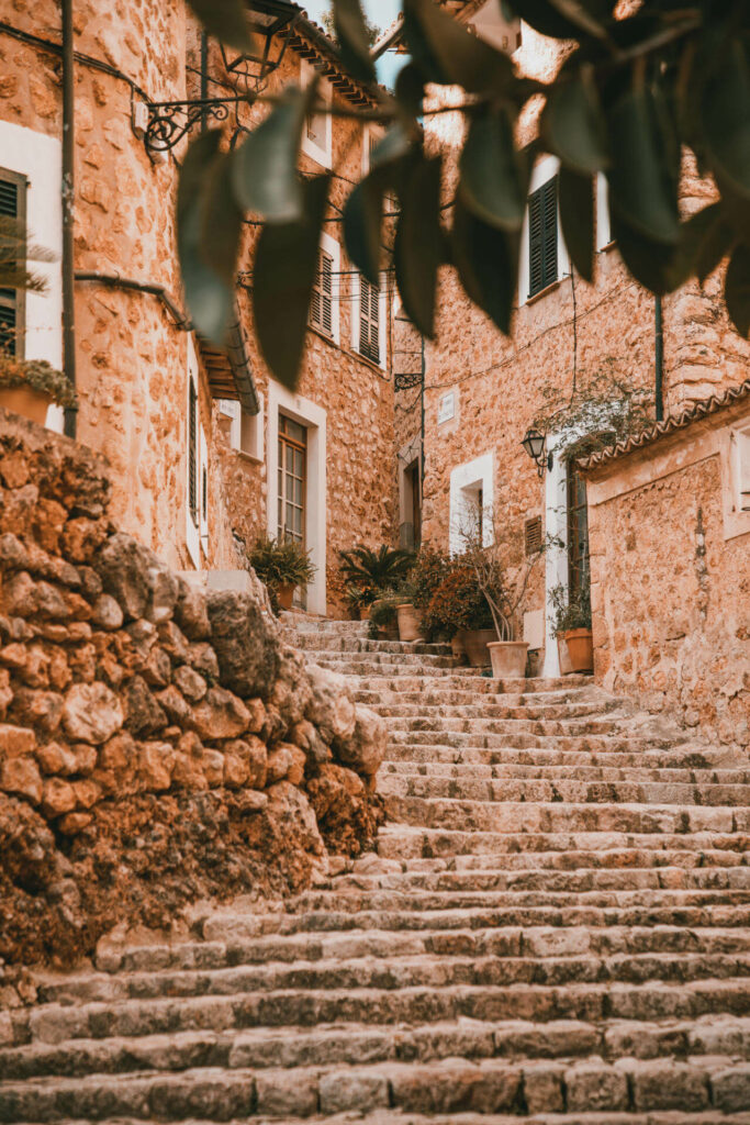 Eine Steintreppe in Fornalutx, die zu einem idyllischen Gebäude hinaufführt, umrahmt von Blättern, zieht sich romantisch durch eines der schönsten Dörfer Mallorcas.