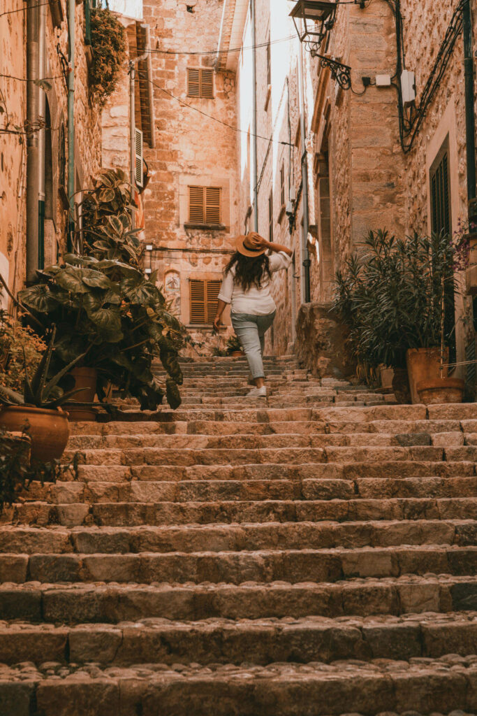 Reisebloggerin Tatiana von Thehappyjetlagger steigt die Stufen einer kleinen bewachsenen Gasse in Mallorcas schönem Dorf Fornalutx hinauf.