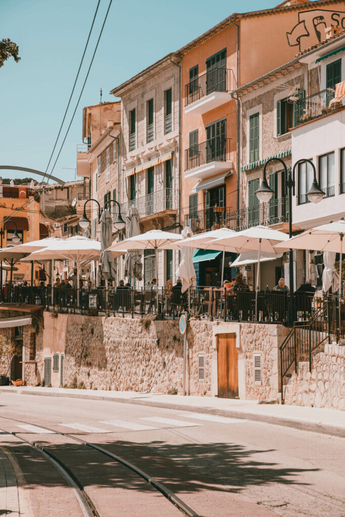 Eine belebte Straße mit Terrassen, die den Berg hinaufführt, bietet den perfekten Blick über den Hafen des Dorfs Sóller auf Mallorca.