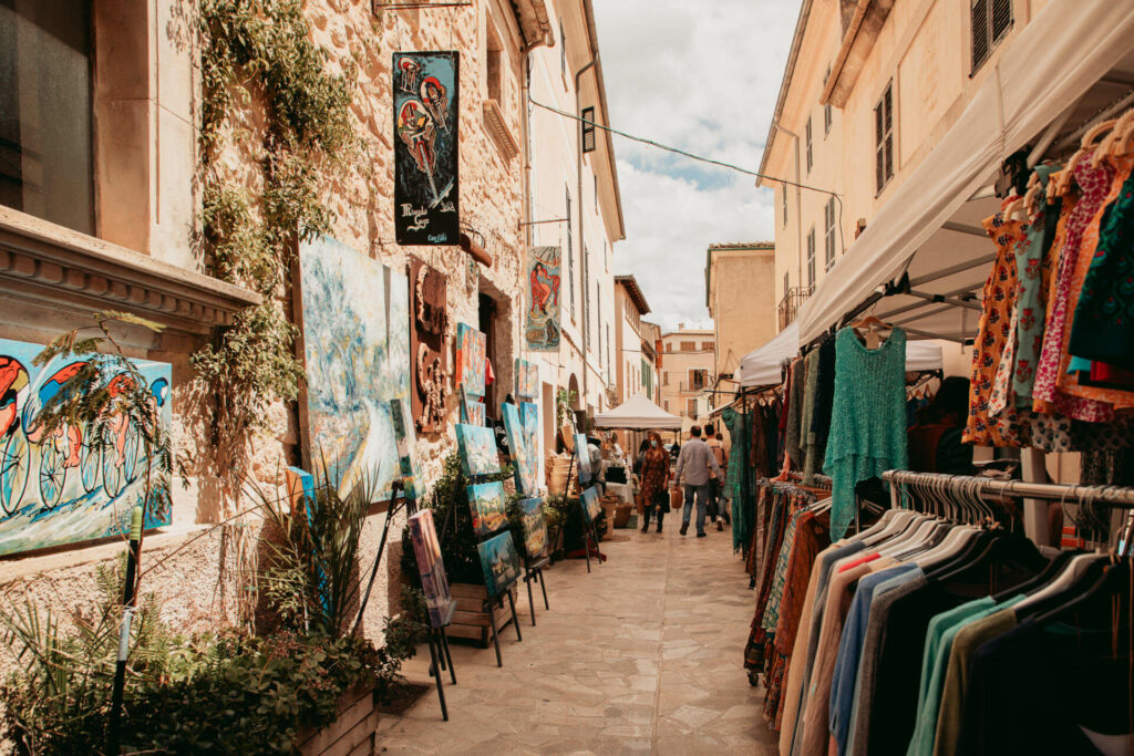 Gemälde und Kleidung ausgestellt für den Verkauf auf dem Wochenmarkt im Dorf Sineu auf Mallorca.