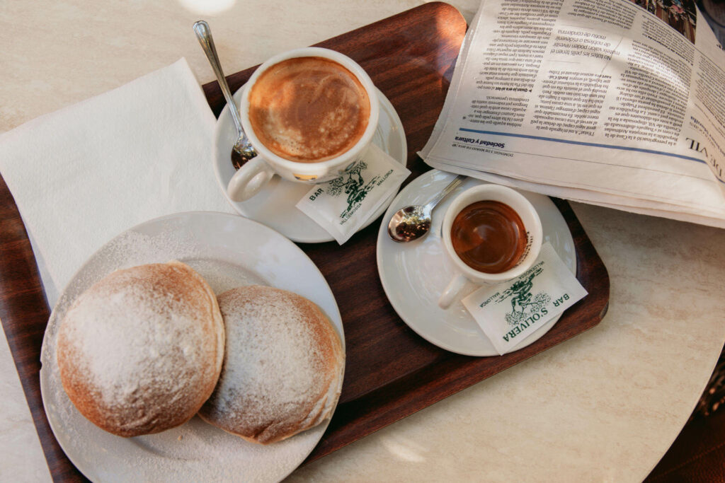 Hefebrötchen aus Kartoffelmehl, Cocas de Patata, mit Kaffee werden auf einem Holztablett in Mallorcas Ort Valldemossa serviert.