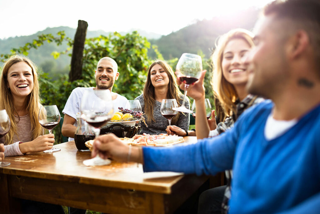 Eine Gruppe von jungen Menschen, die zusammen draußen fröhlich Wein trinken