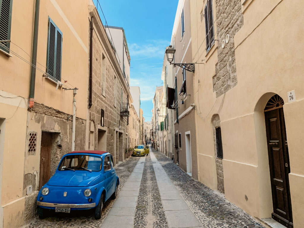 Ein süßes blaues Auto parkt in einer Straße der Altstadt von Alghero im Norden von Sardinien.