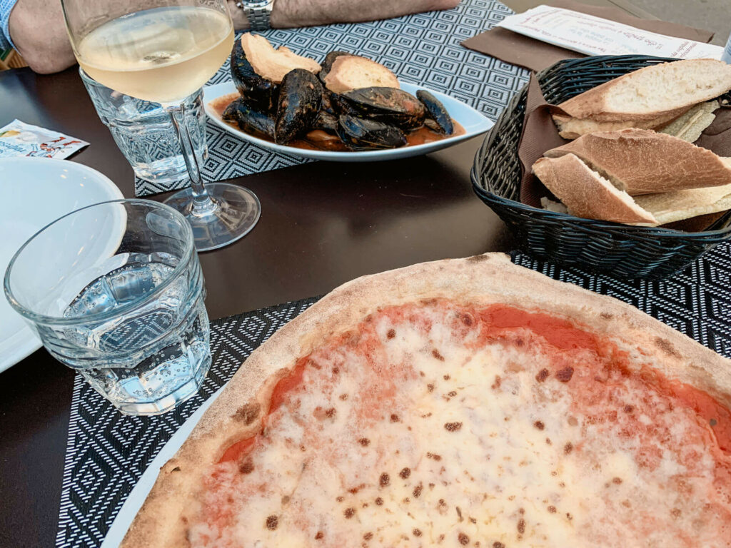 Eine Pizza von Pepebianco auf Sardinien mit Baguette, Muscheln und Wein.