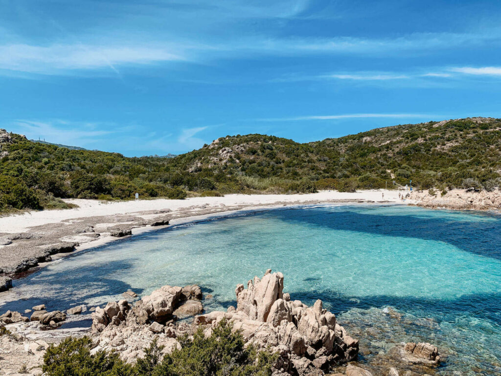 In der Bucht an der Spiaggia del Principe in Sardinien ist das strahlend blaue Wasser von Strand und Bergen umgeben.