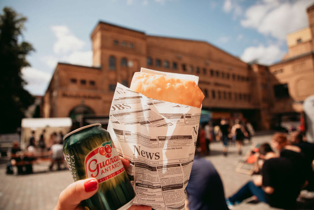 Brasilianische Pasteis und Guaraná werden vor der Kulturbrauerei hochgehalten.