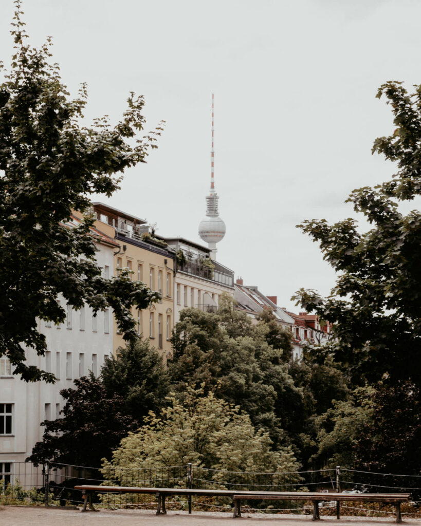 Die Aussicht vom Park oberhalb des Wasserturms auf den Berliner Fernsehturm zwischen den Häusern und Bäumen.