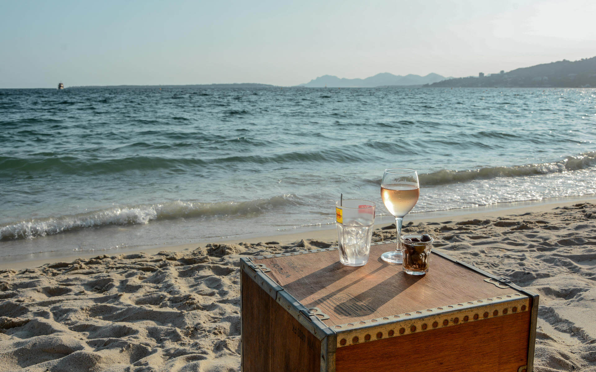 Kiste mit Vino am Strand vor Meereskulisse.