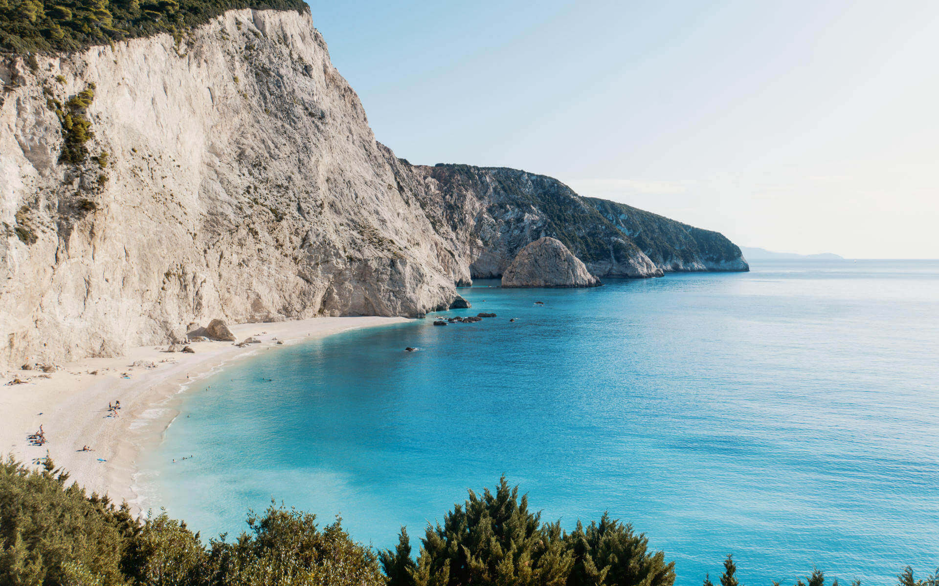 Hohe Wände aus Kalkfelsen umrahmen die traumhafte Bucht von Porto Katsiki auf der griechischen Insel Lefkada. Besucher sonnen sich am feinen Sandstrand, ein paar von ihnen baden in dem türkisblauen Wasser des Ionischen Meers.