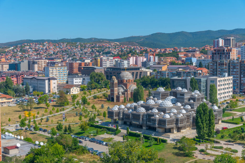 Pristina, eine Stadt umgebe von Grünflächen und Bergen.