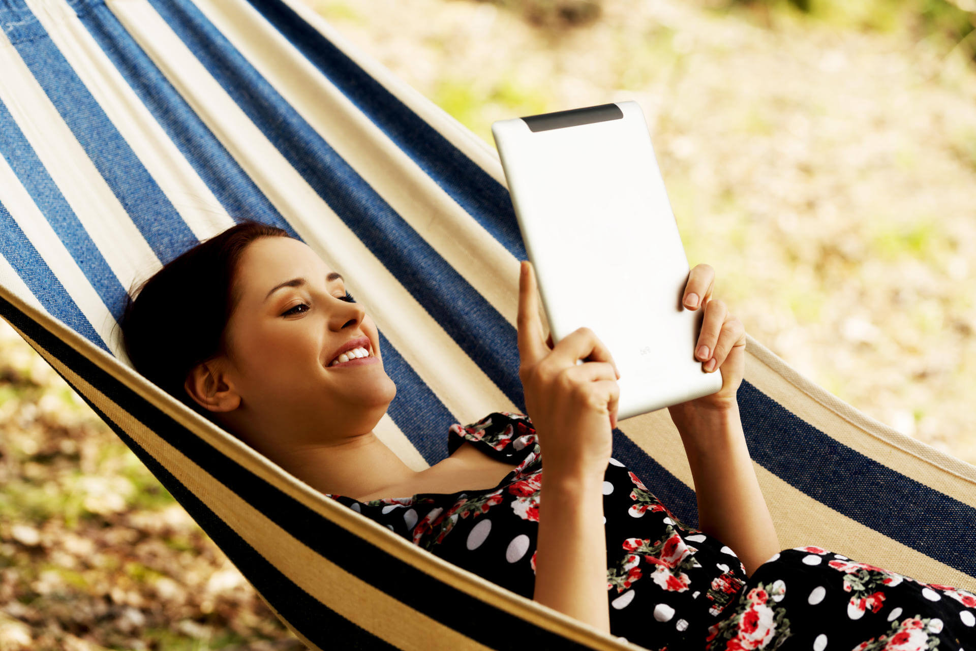 Eine Frau lächelt, während sie von der Hängematte aus ihr eBook liest.