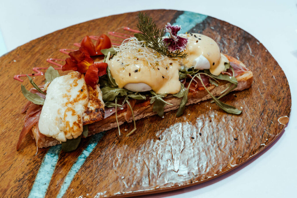 Beim Crustina Eggullera, was in der Eixampeling Brunch Café & Bar in Barcelona serviert wird, gibt es eine getoastete Scheibe Brot mit Serrano Schinken, pochierten Eiern, Sauce Hollandaise, Rucola und Tomaten.
