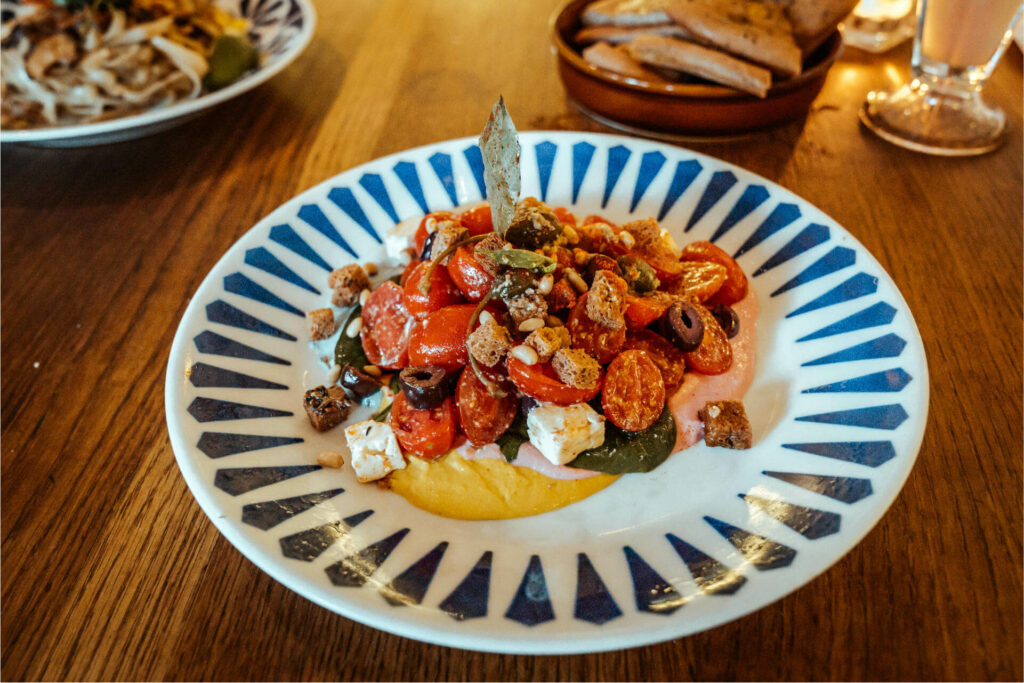 Der Salads for the Gods von Flax & Kale in Barcelona mit mit Spinat, Cherrytomaten, Kalamata Oliven, Kapern und Nüssen auf regenbogenfarbenem Hummus ist nicht nur wunderschön, sondern auch gesund und köstlich.