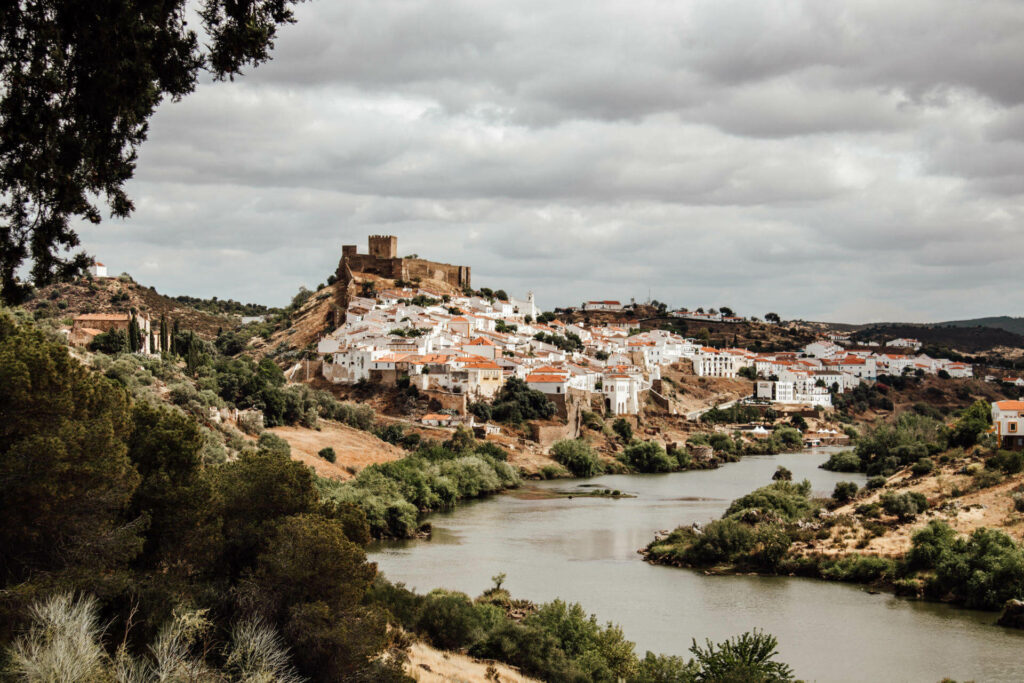 Eine Sehenswürdigkeit im Alentejo: Mértola. Ein sich schlängelnder Fluss vor dem Hügel einer Stadt im Alentejo.