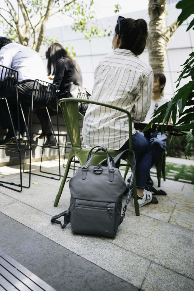 Eine Reisende kann dank des nützlichen Reise-Gadgets von Pacsafe ihren Rucksack am Stuhl befestiegen.