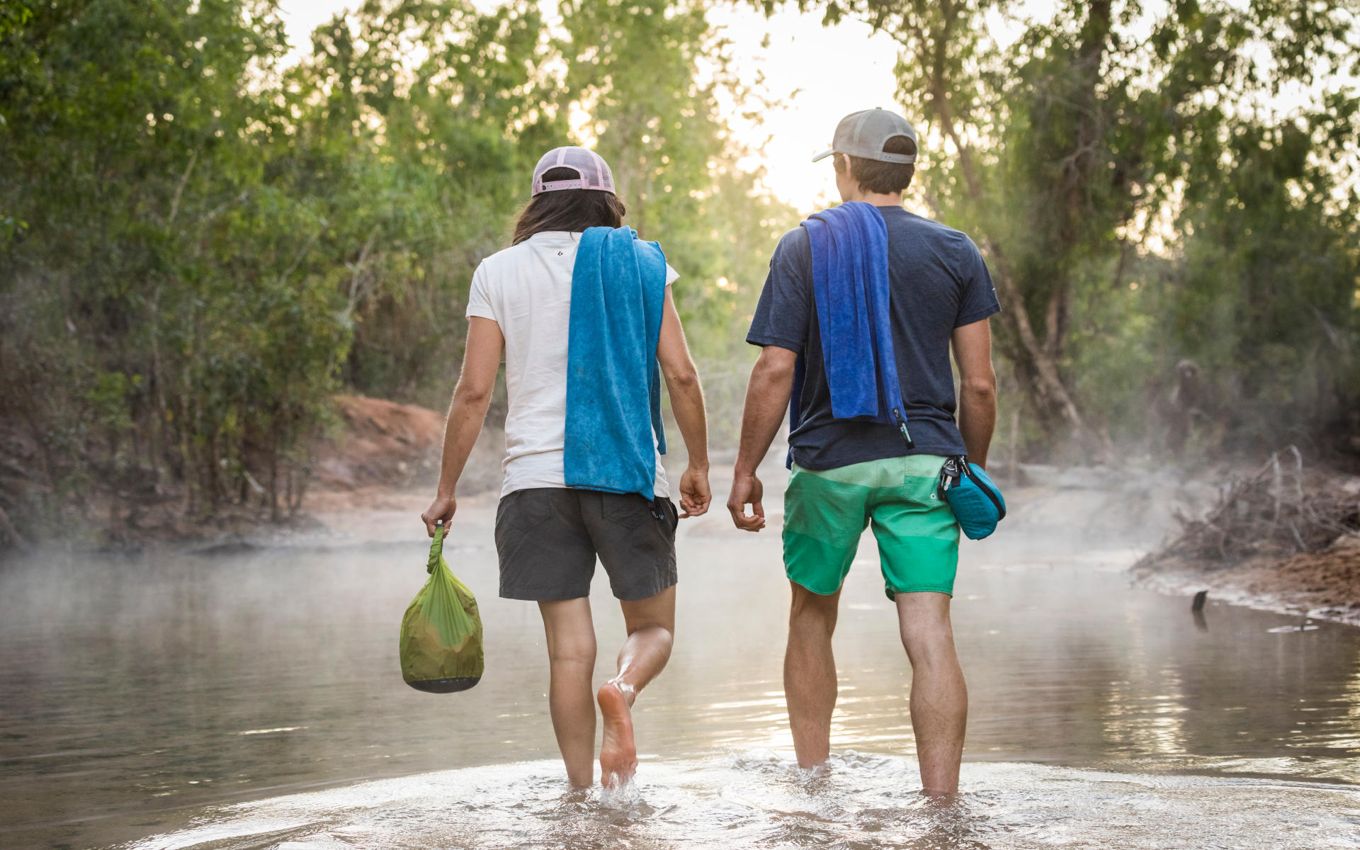 Zwei Reisende schlendern durchs Wasser, dabei einen Dry Bag, um die wertvollsten Gegenstände trocken zu halten - ein wahnsinnig nützliches Gadget auf Reisen.