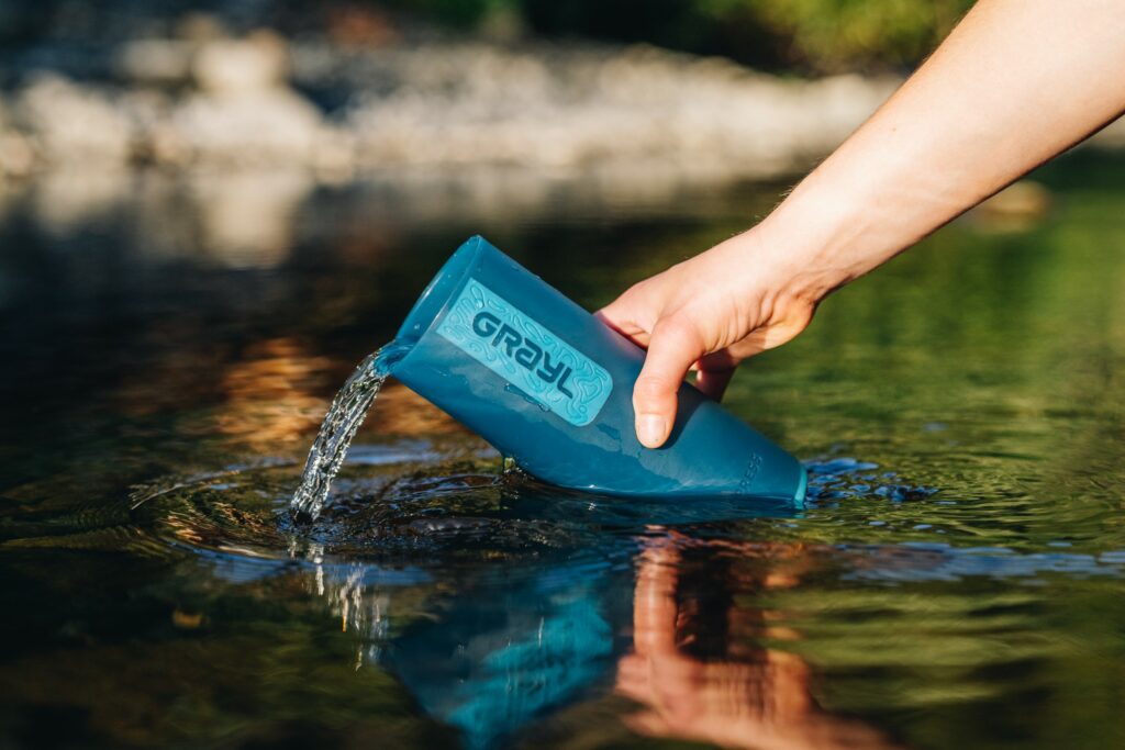 In natürlichem Gewässer lässt sich mit dem praktischen Wasserfilter von Grayl Wasser auf Reisen filtern.