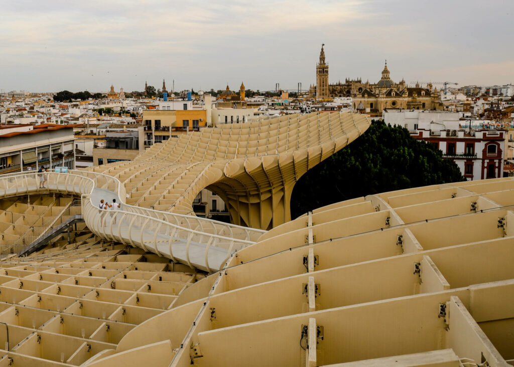 Eine Brücke führt über ein künstlerisches Gebilde über den Dächern von Sevilla hinweg.