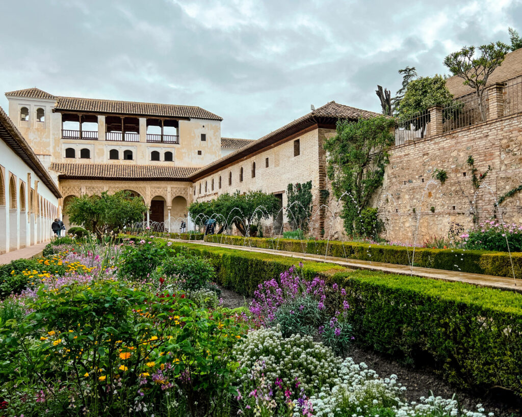 Ein farbliches Zusammenspiel aus grünen Hecken und gelb, rosa und weißen Blumen lassen den Palast im Generalife in der Alhambra erstrahlen.