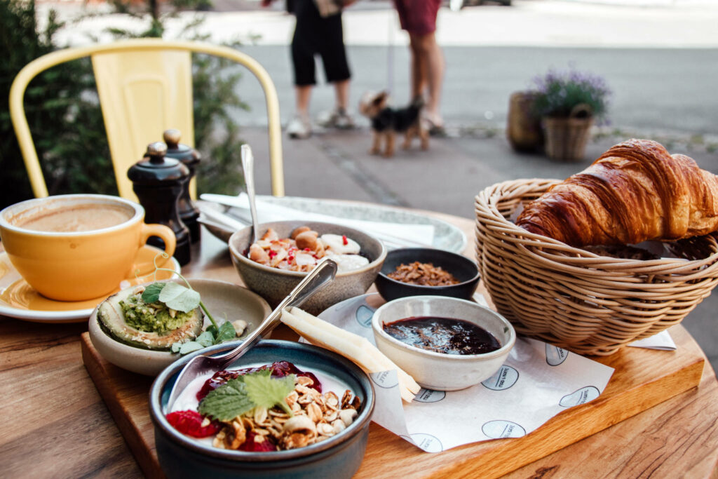 Das Frühstück mit Kaffee, Croissant, Avocado und Joghurt mit Müsli wird im Café Mad & Kaffe auf einem Holzbrett serviert.