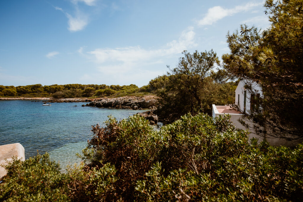 Ein mallorquinische Haus in weiß umgeben von wildwachsenden Bäumen mit Blick auf das Meer in der Bucht Es Carregador.