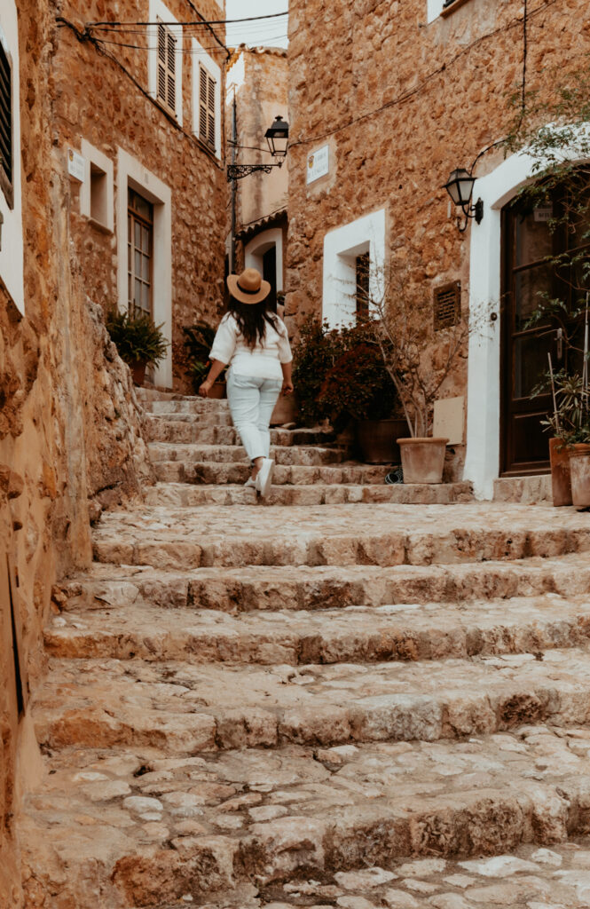 Eine Frau mit Hut läuft die steinernen Treppen zu den Häusern im Ort Fornalutx hoch.