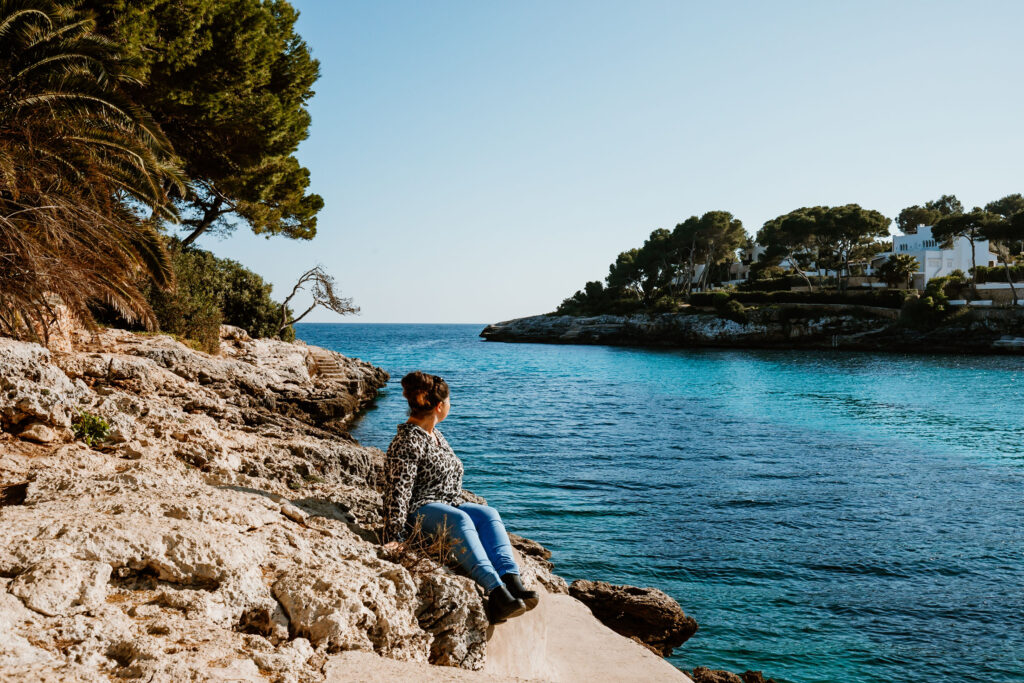 Eine Frau sitzt an einer Steinküste von Mallorca mit Blick aufs Meer