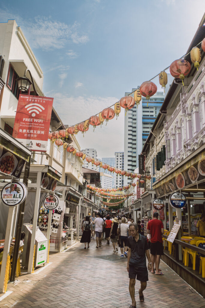 Gewusel in einer engen Straße und Lampions, die zwischen Gebäuden hängen in Chinatown in Singapur.