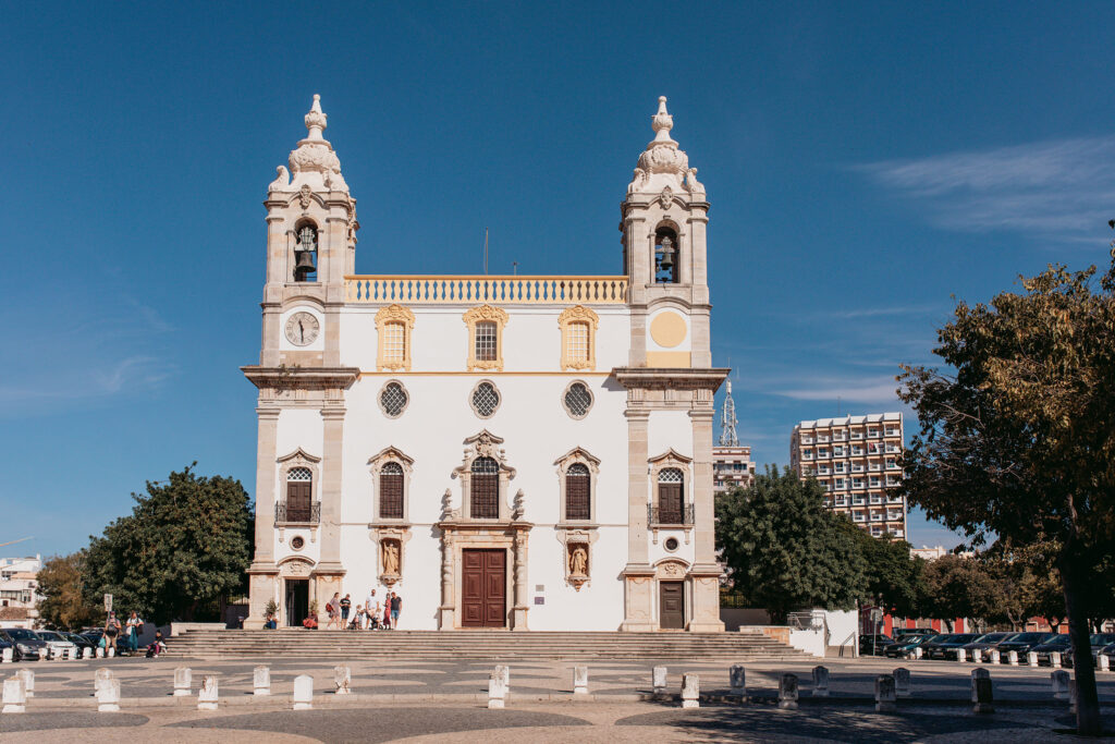 Die barocke weißfarbene Kirche "Igreja do Carmo" mit 2 Türmen in Faro ragt in den blauen Himmel.