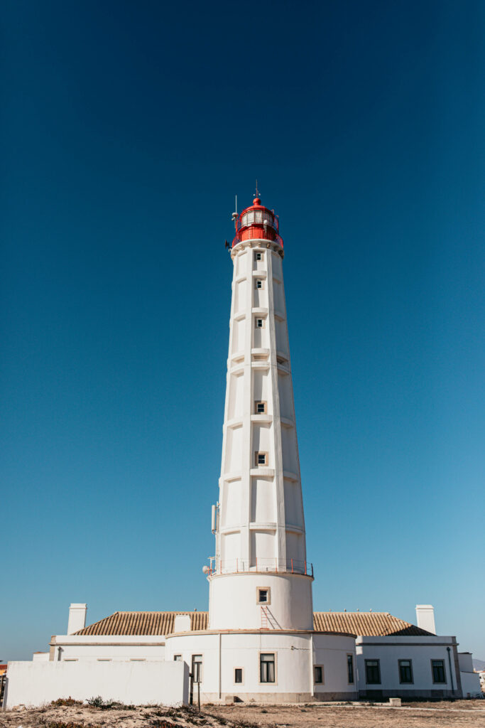 Der weiße Leuchtturm mit dem roten Dach ragt auf der Ilha do Farol in den strahlend blauen Himmel.