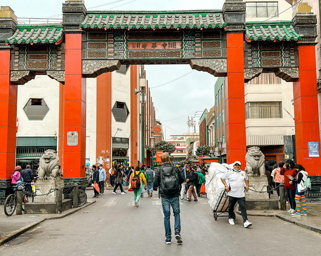 Ein Tor mit roten Säulen und einem grünem Dach das den Weg Richtung Chinatown in Lima öffnet.