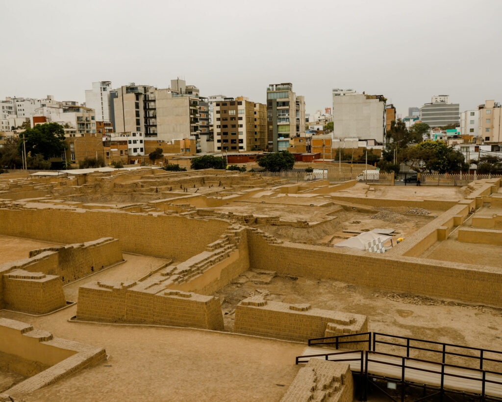 Eine alte sandfarbene Ruine inmitten der Stadt von Lima und umgeben von Wohnhäusern.