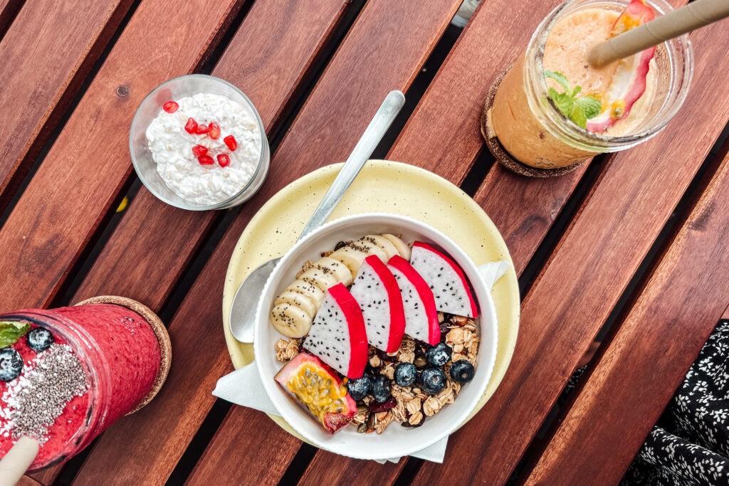 Eine Acai Bowl sowie zwei Smoothies stehen auf einem Holztisch.