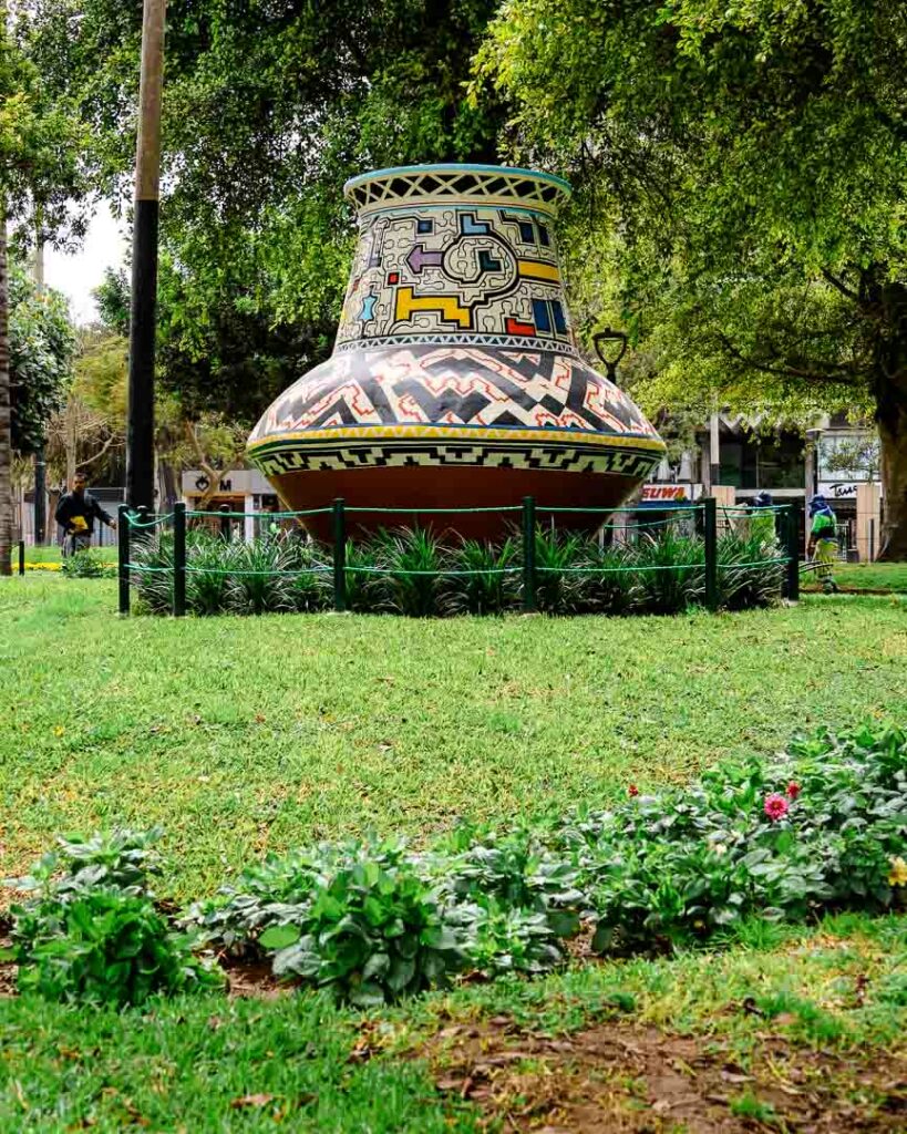 Eine saftgrüne Wiesenfläche im Kennedy Park in Lima mit einer riesigen Tonvase mit bunten Mosaiksteinen besetzt.
