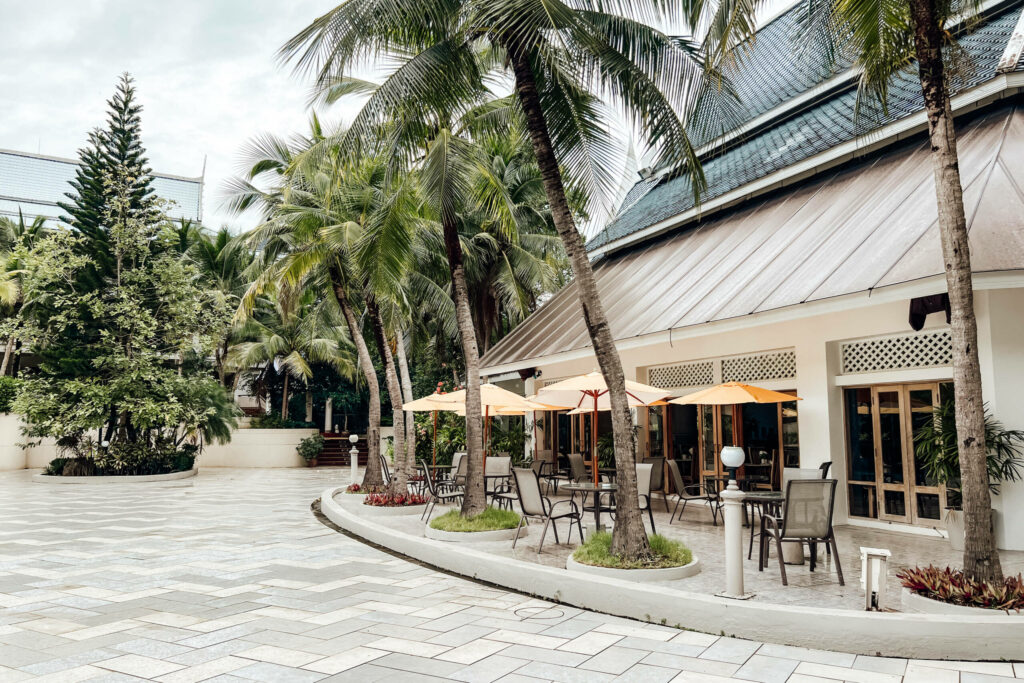 Der palmengesäumte Außenbereich des Chada Thai Village Resort in Krabi mit Tischen, Stühlen und gelben Schirmen.
