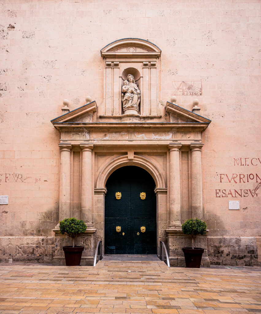 Entrance of a church with a black door and a figure of Mary in the old town of Alicante.