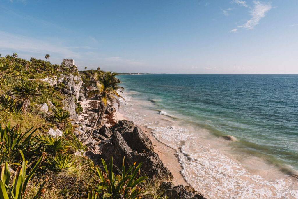 Eine grünbewachsenen Felsküste bei den Ruinen in Tulum auf Yucatan verzaubert mit blau strahlendem Meer.