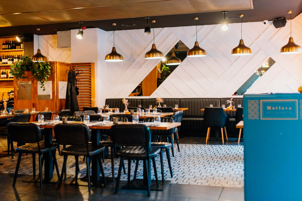 Das modern eingerichtete Restaurant Motlava in Danzig schmücken schwarze Stühlen, Holztischen und goldene Hängelampen.