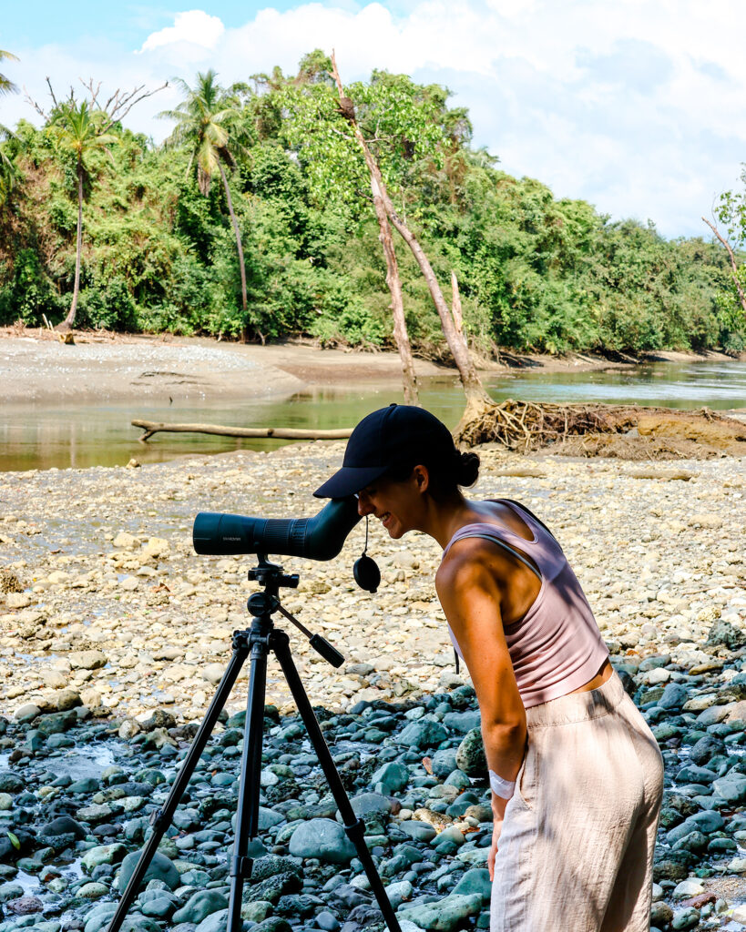Blogger Nina stands on the stone beach in Corovado National Park and looks through a monocular.
