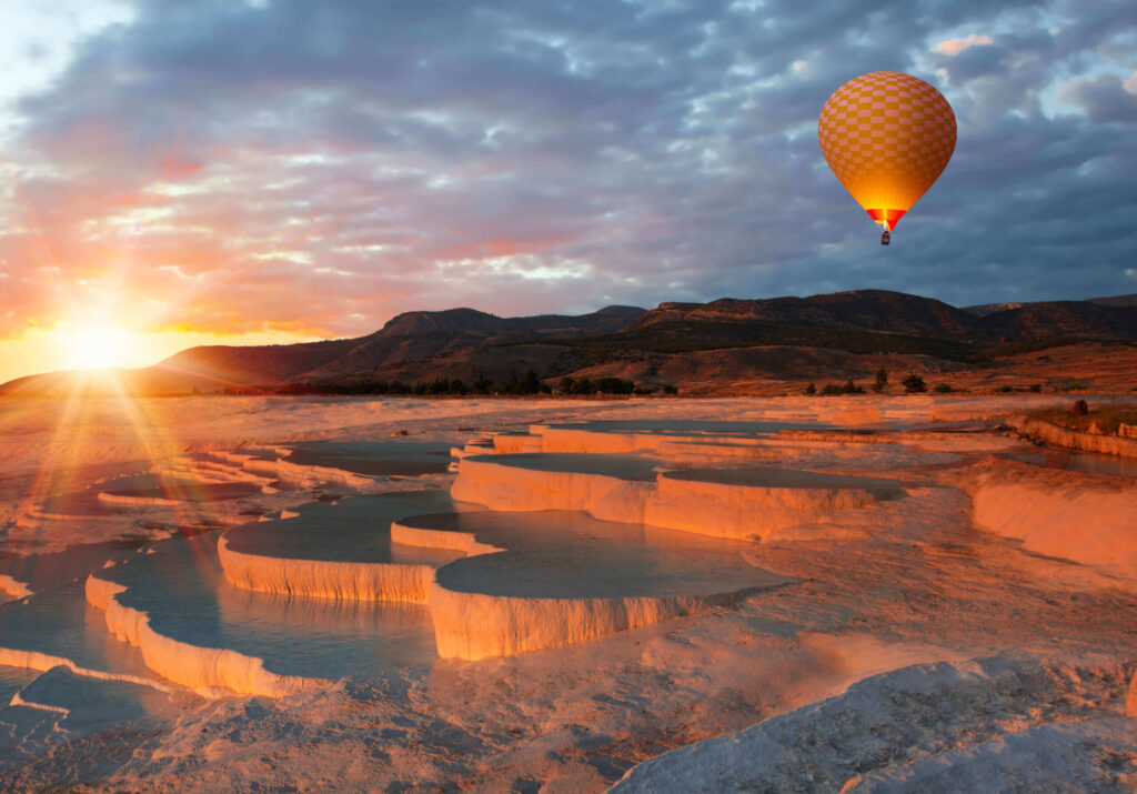 Ein Heißluftballon bei Sonnenuntergang über den Terrassen von Pamukkale.