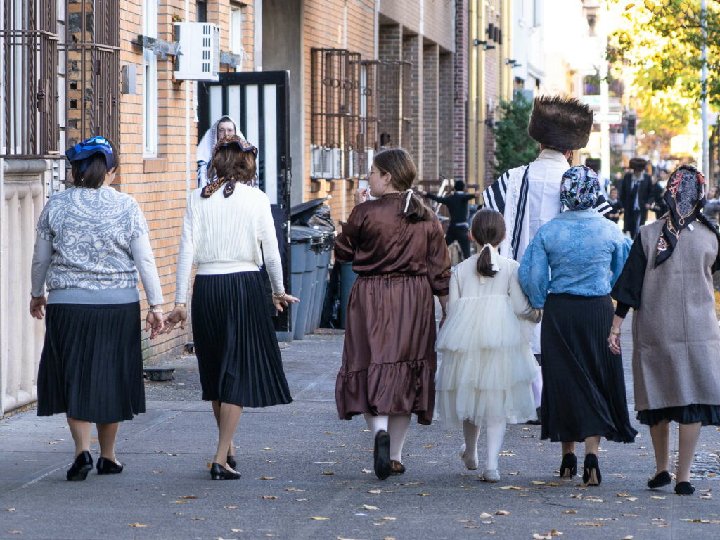 A group of Hasidic Jewish women wearing traditional dress and headscarves walk down a street in the Williamsburg neighborhood of Brooklyn.