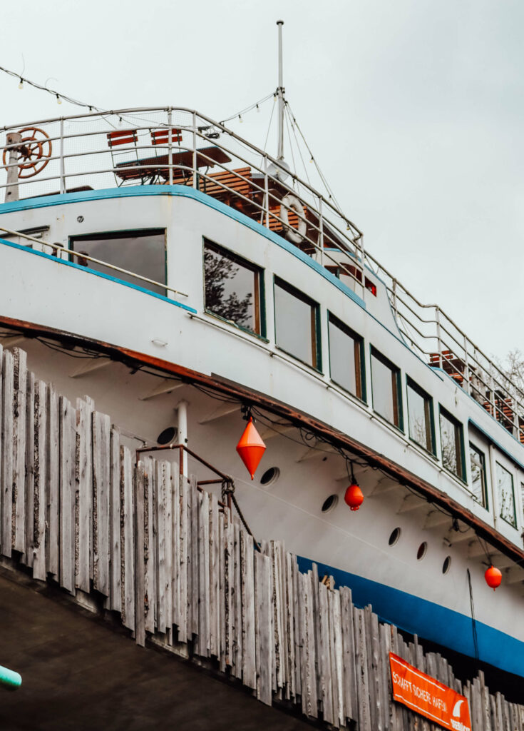 Ein altes Schiff mit Stühlen und Tisch an Deck auf einer Brücke - die Alte Utting in München.