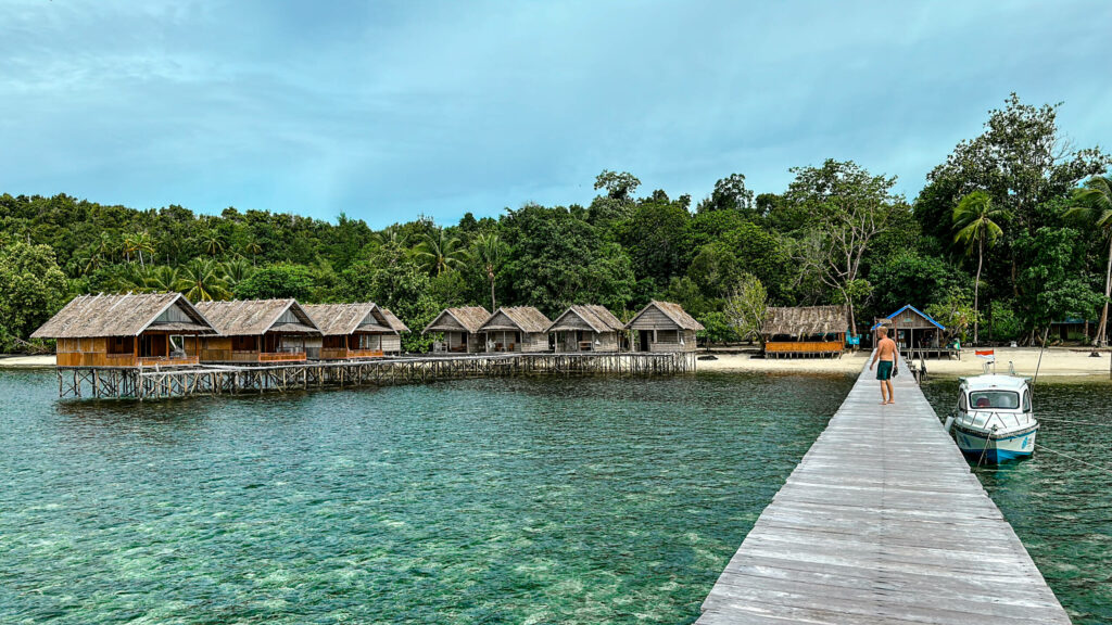 Blogger Tom steht auf einem Holzsteg und blickt auf die Over-Water-Bungalows eines Homestays auf Raja Ampat.